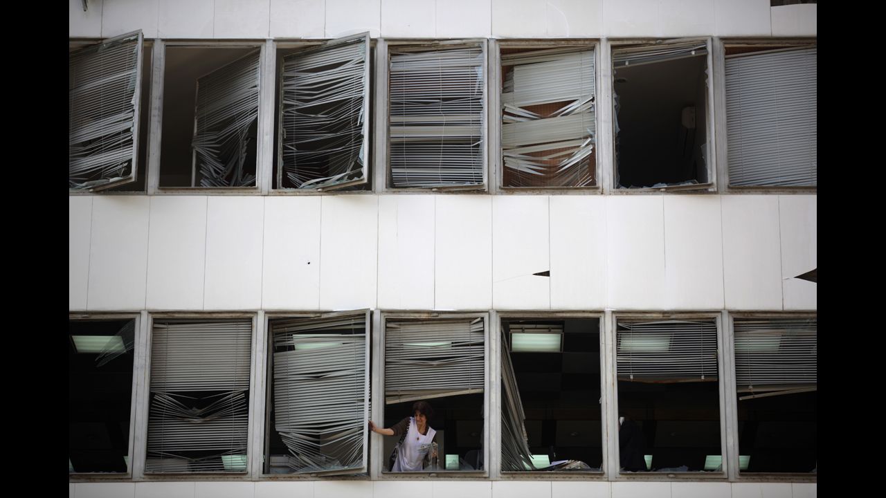 A woman removes shattered windows as she cleans an office near the site.