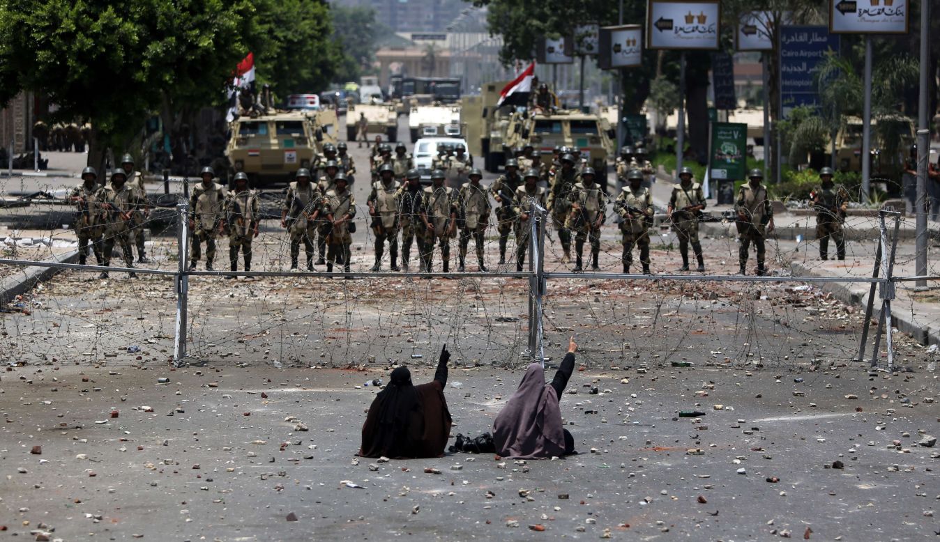 Two veiled Egyptian women, supporters of Mohamed Morsy, sit in front of police standing behind barbed wire fencing that blocks the access to the headquarters of the Republican Guard in Cairo on July 8, 2013. 