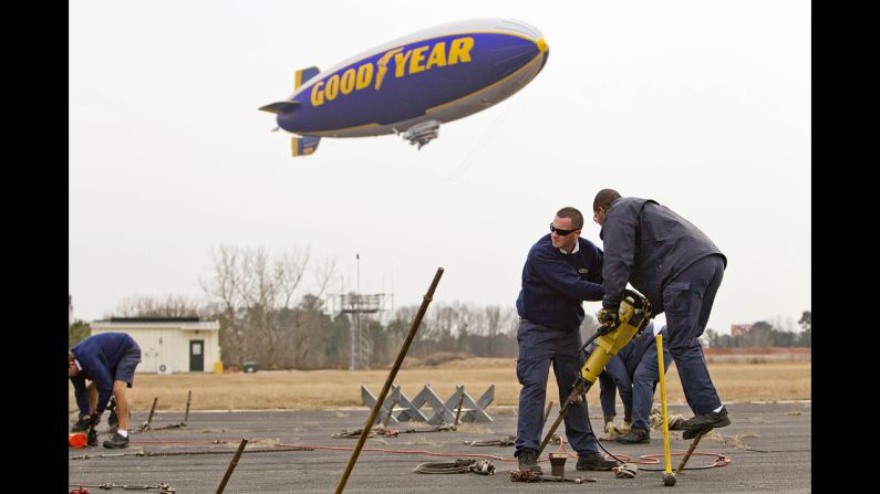 The Goodyear blimp Spirit of Innovation arrived in Atlanta on December 30 to prepare for its New Year's Eve flight above the Chick-fil-A Bowl. Aaron Hullander, left, and Olenskian Spoon carry a jackhammer to secure posts as the Goodyear Blimp comes in for a landing at DeKalb-Peachtree Airport.