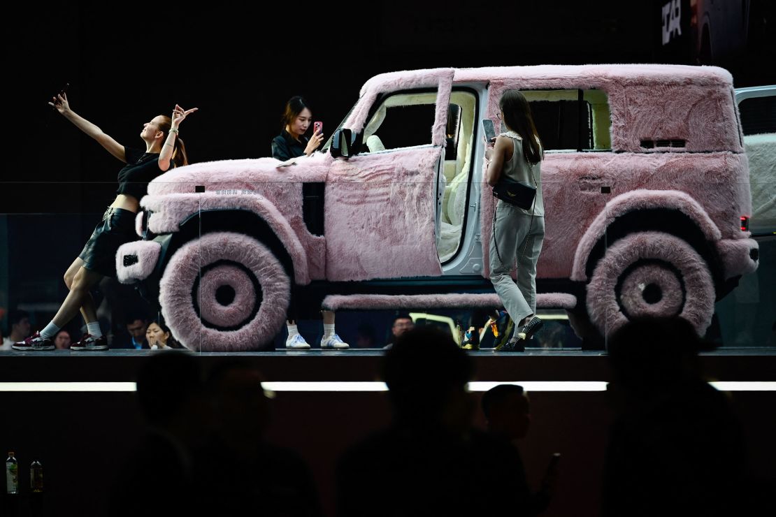A woman takes a selfie with a fur-covered iCAR V23 at the auto show.