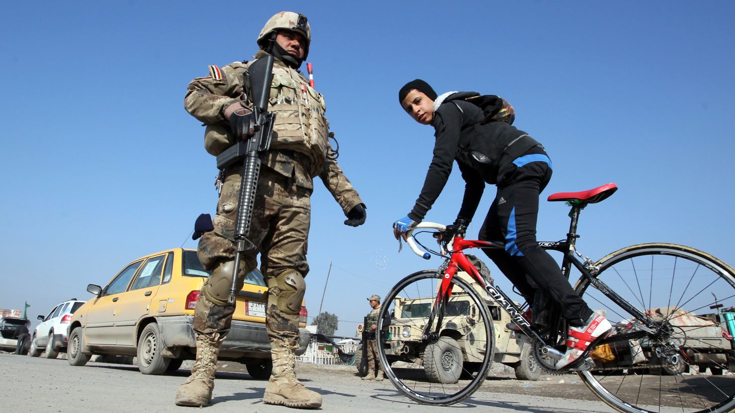A boy cycles past Iraqi soldiers monitoring a checkpoint east of Baghdad on January 6, 2014.