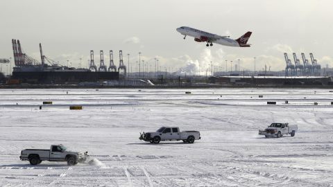 A plane takes off from Newark Liberty International Airport in Newark, New Jersey, as trucks plow snow on the tarmac January 3.
