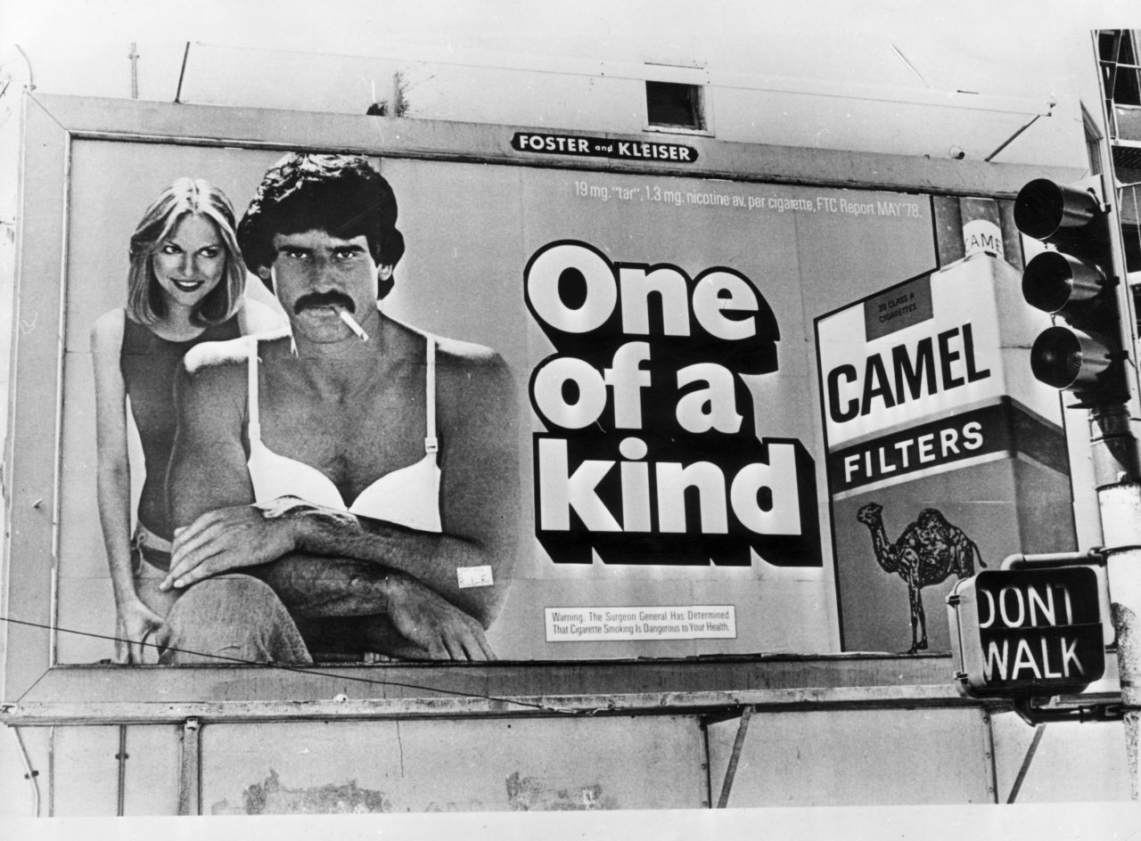 A giant bra was added to this Camel ad in San Francisco by Billboard Liberation Front members who objected to the use of male bodies in ads. At the bottom of the billboard is the surgeon general's warning, which  were added to cigarette ads soon after Terry's report in 1964.