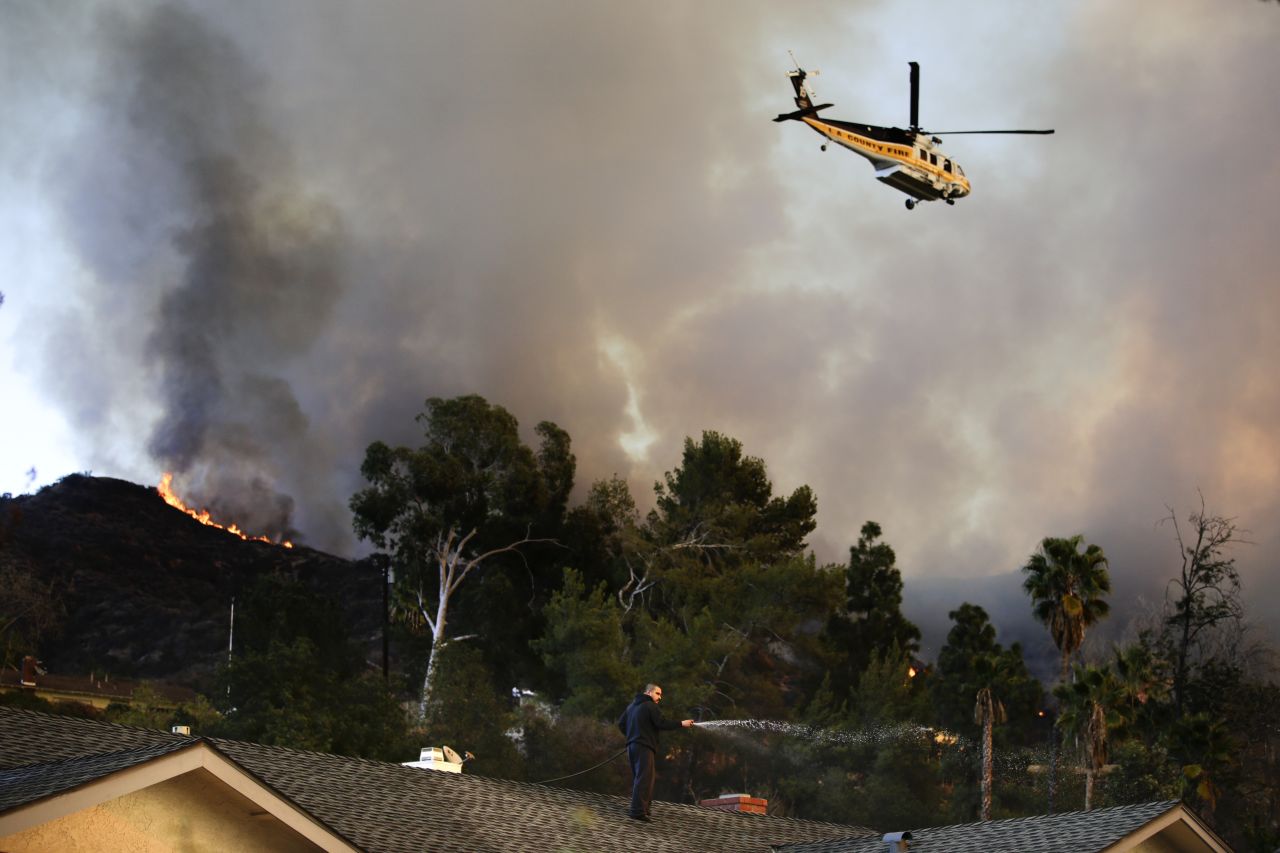 A helicopter carrying water flies over a burning residential area in Azusa, California, as a man sprays water on his home January 16.