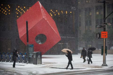 People walk past the art installation "Red Cube" by Isamu Noguchi in New York during a snow storm on January 21.