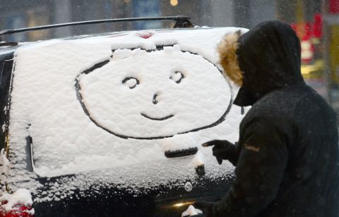 A person draws a happy face in the snow on a car window in New York.