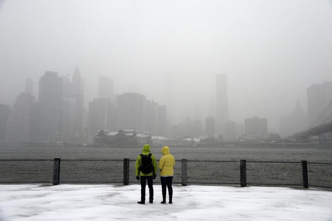 Snow falls as tourists take in the New York skyline from the Brooklyn Bridge Park on January 21.