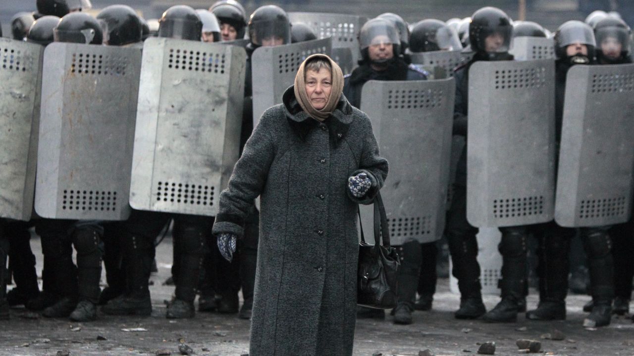 An elderly woman walks from police officers as they block a street during unrest in central Kiev, Ukraine,Tuesday, Jan. 21, 2014.