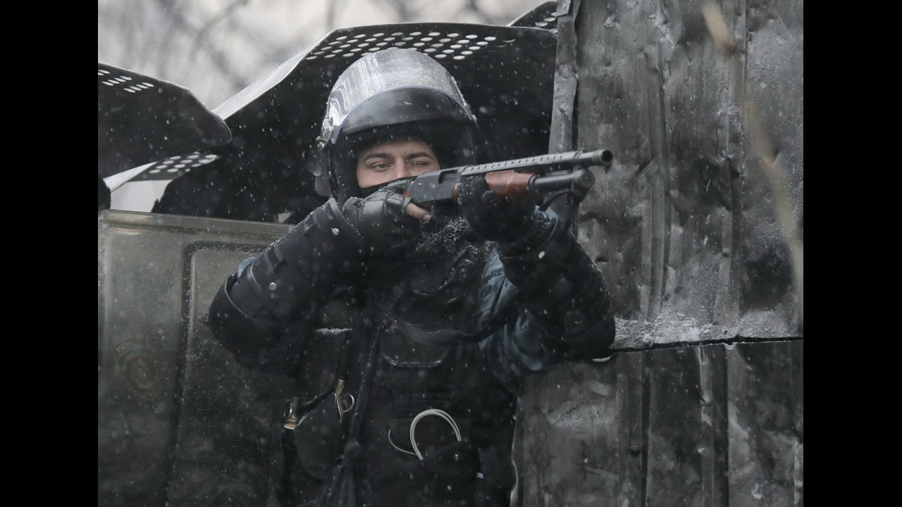 A police officer aims his shotgun during clashes with protesters.