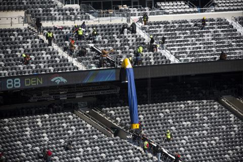 Workers remove snow from the stands. Cold-weather welcome kits have been produced for fans. They will include earmuffs, hats, mittens and lip balm, among other items.