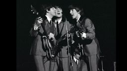The Beatles 1964 US Tour, L-R: Paul McCartney, John Lennon and George Harrison share a microphone as they sing a song in concert at Carnegie Hall in New York during the band's tour of America  (Photo by Popperfoto/Getty Images)