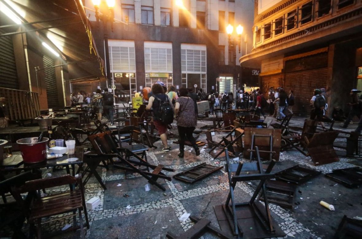 People walk among tables and chairs trashed during the protest.