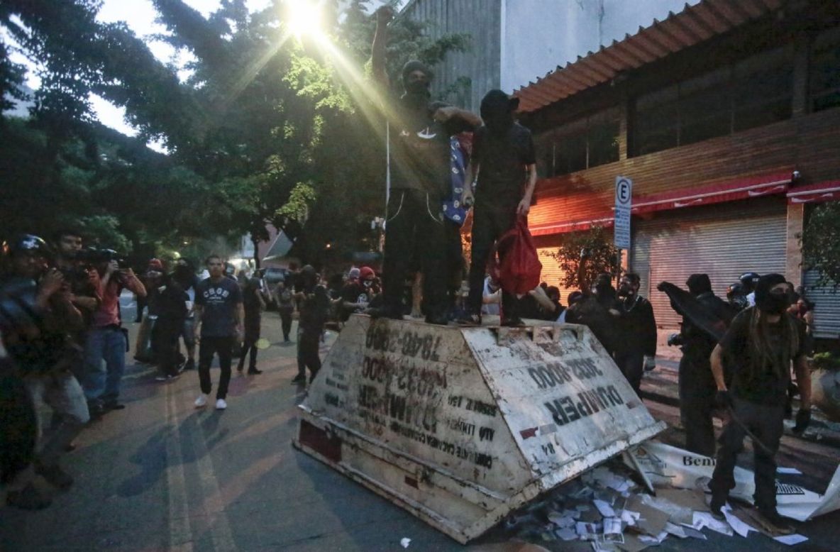 Demonstrators stand on top of an overturned garbage container.