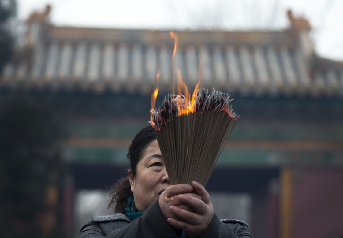 A woman holding incense prays at the Yonghegong Lama Temple. In China, the festivities are also known as the spring festival.