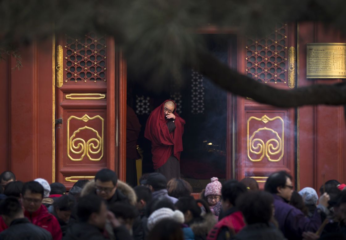 A monk stands at the entrance to the Yonghegong Lama Temple as people pray on the first day of the Lunar New Year.