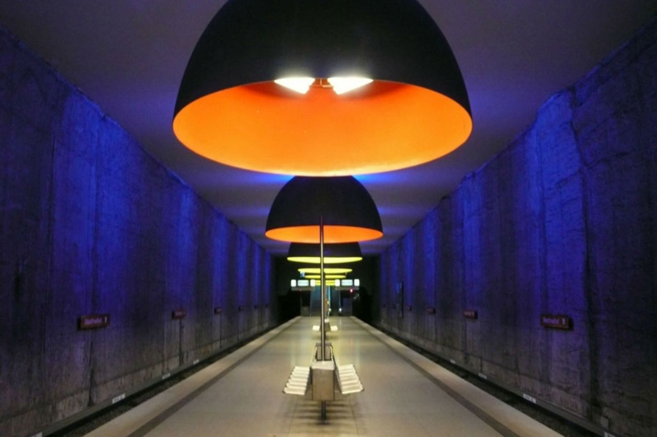 Las enormes luces del domo que envuelven las plataformas en tonos inquietantes de azul, rojo y amarillo hacen que la estación de Westfriedhof en Múnich, la cual de otra manera se vería ordinaria, ruja.