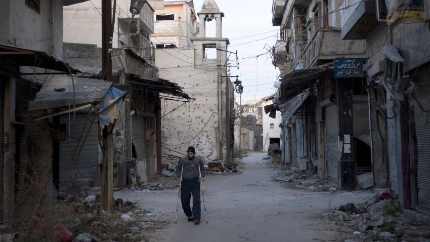 A man uses crutches as he walks past damaged buildings in a neighbourhood, besieged by government forces, in the central Syrian city of Homs on February 1, 2014.