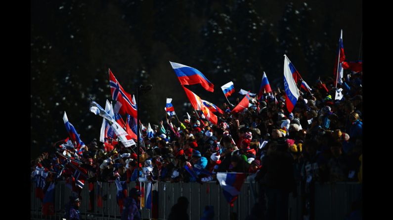 Spectators wave national flags close to the finish line of the women's skiathlon.