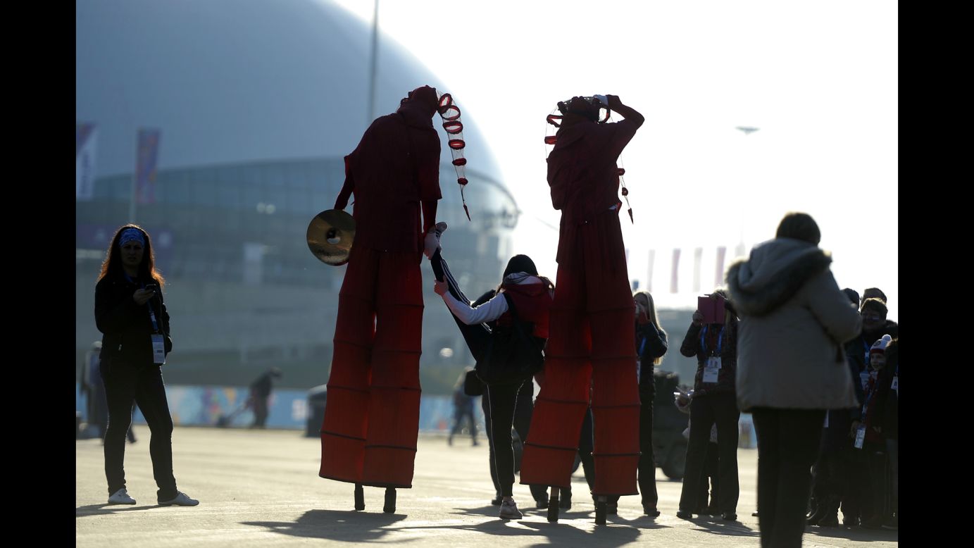 A pair of street performers on stilts help a young woman stretch February 8 at the Olympic village.