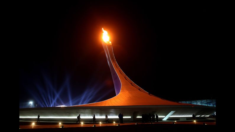 The Olympic flame burns in the cauldron February 8 as people walk in Olympic Park.