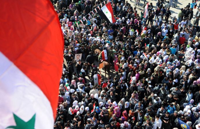 En esta foto del folleto publicado por la Agencia oficial de Noticias Árabe Siria el 8 de febrero, los civiles ondean banderas nacionales en Damasco, mientras participan en una concentración en apoyo al Presidente al-Assad. 