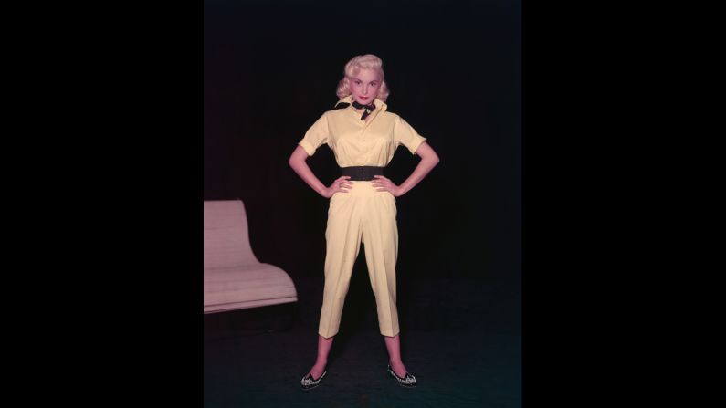 Actress Janet Leigh models a yellow short-legged jumpsuit with a wide belt, beaded shoes, and a neckerchief in the 1950s.