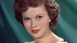 circa 1955: Headshot studio portrait of American actor Shirley Temple, in front of a green backdrop, wearing a short sleeve white blouse with a colored bows pattern and a pearl necklace. (Photo by Hulton Archive/Getty Images)