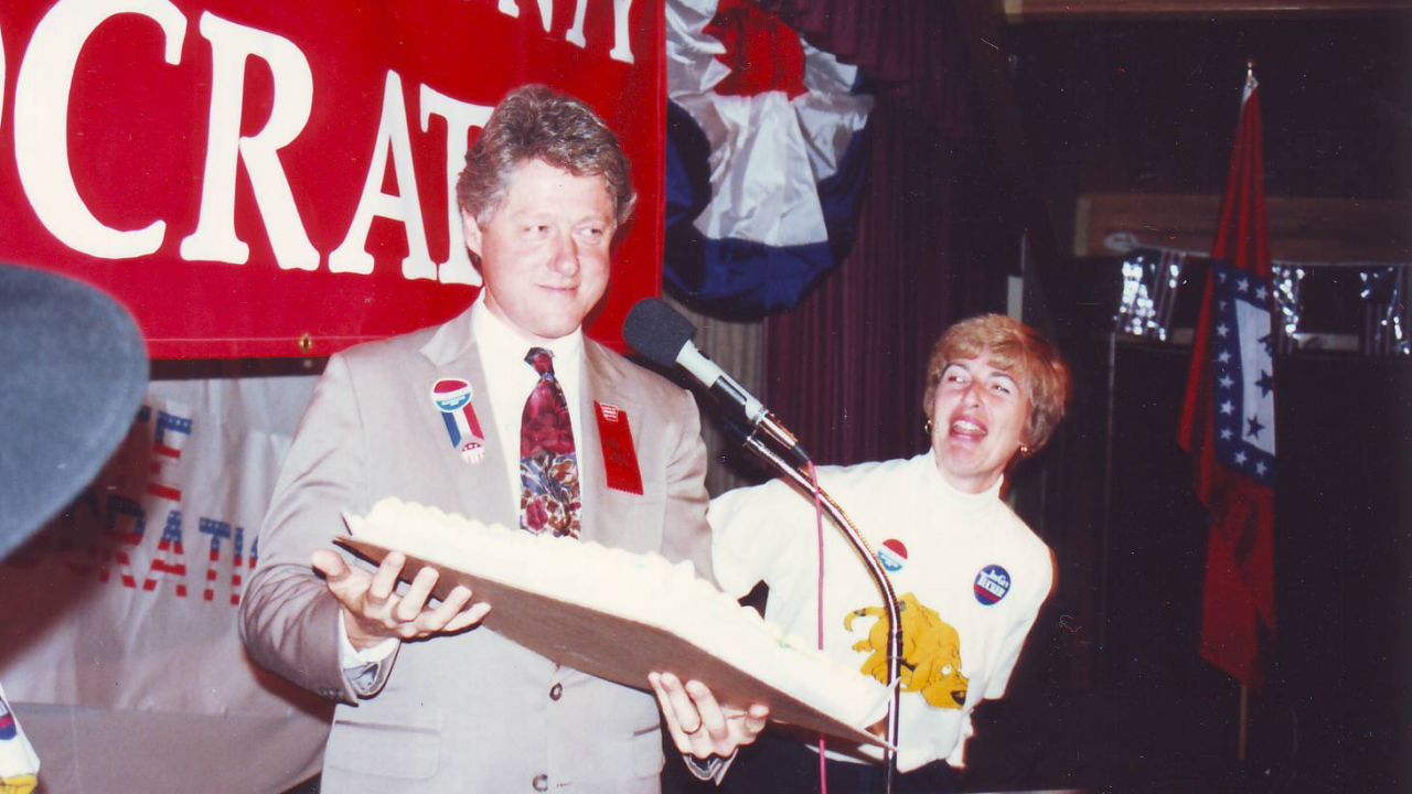 Diane Blair looks amused as Bill Clinton holds a cake at a 1988 Democratic event in Washington County, Arkansas.