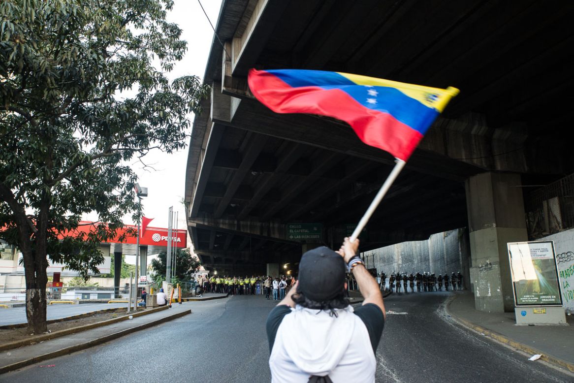 Un estudiante frente a los efectivos de seguridad ondea la Bandera Nacional de Venezuela durante las protestas del 15 de febrero en Caracas.