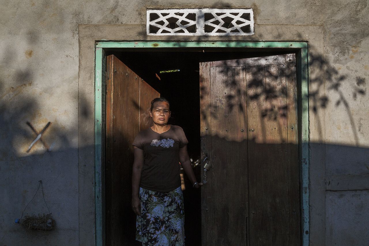 A widow stands in the doorway of her home. She lost her husband and two brothers to kidney disease.