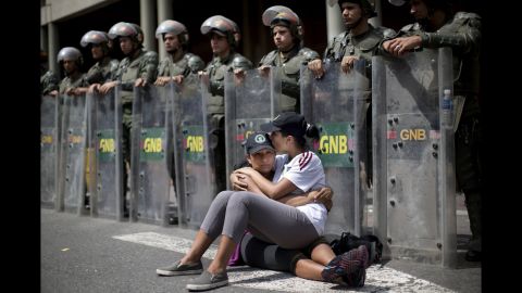 Two women sit in front of a line of National Guard officers outside the Palace of Justice in Caracas on February 19.