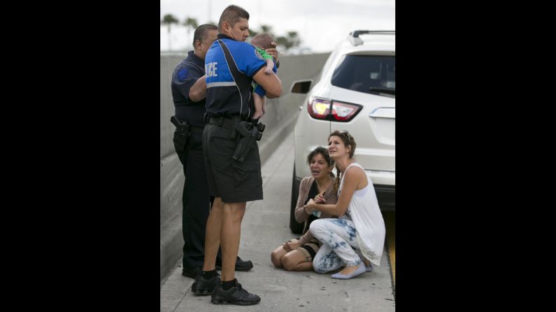 Police officer Amauris Bastidas holds the infant after responding to the scene. At the far right is Lucila Godoy, a woman who stopped her car to assist Rauseo.