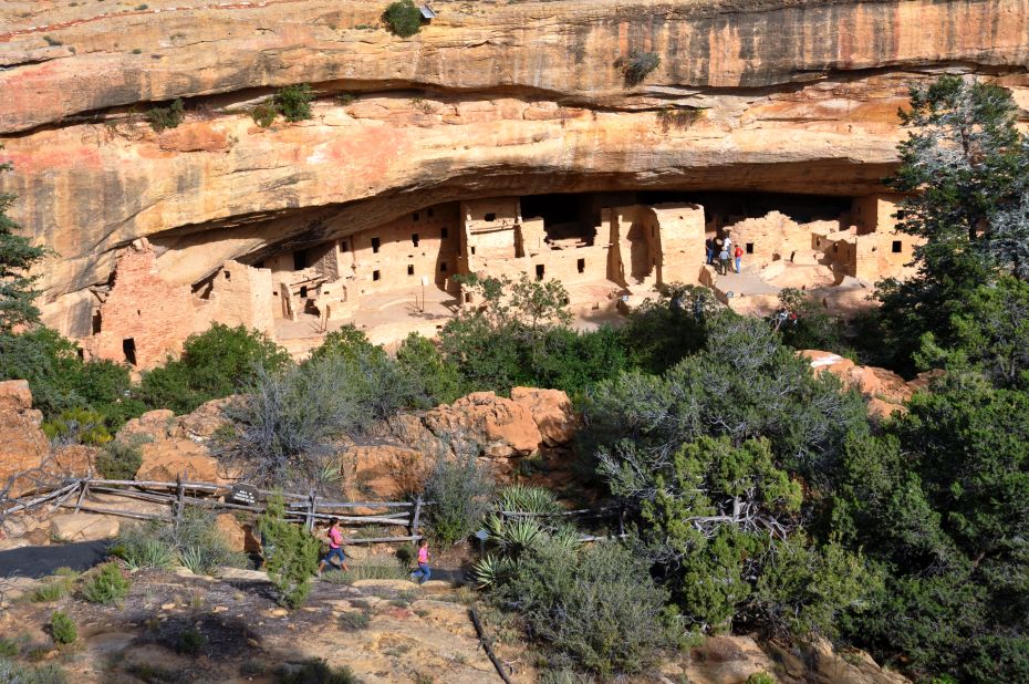 A trail leads visitors to the Spruce Tree House ruins in Mesa Verde National Park. The park's stone and adobe cliff dwellings were built by Ancestral Puebloans from the 1190s to the late 1270s. 