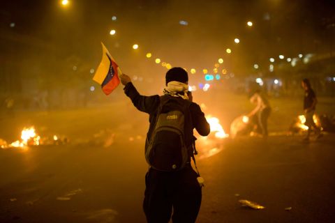 A Venezuelan protester waves a flag in front of a burning barricade in Caracas on Friday, February 21.