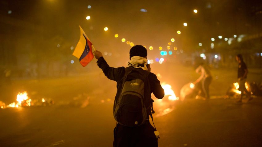 A Venezuelan protester waves a flag in front of a burning barricade in Caracas on Friday, February 21.