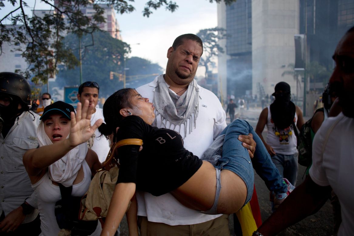 Un hombre carga a una a una mujer afectada por gas lacrimógeno lanzado por la policía para dispersar protestas en Caracas el sábado 22 de febrero.