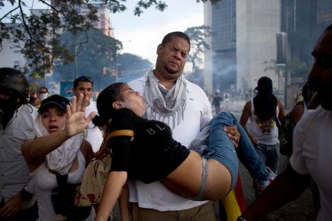 A man carries a woman overcome by tear gas that was fired at anti-government protesters in Caracas on Saturday, February 22.