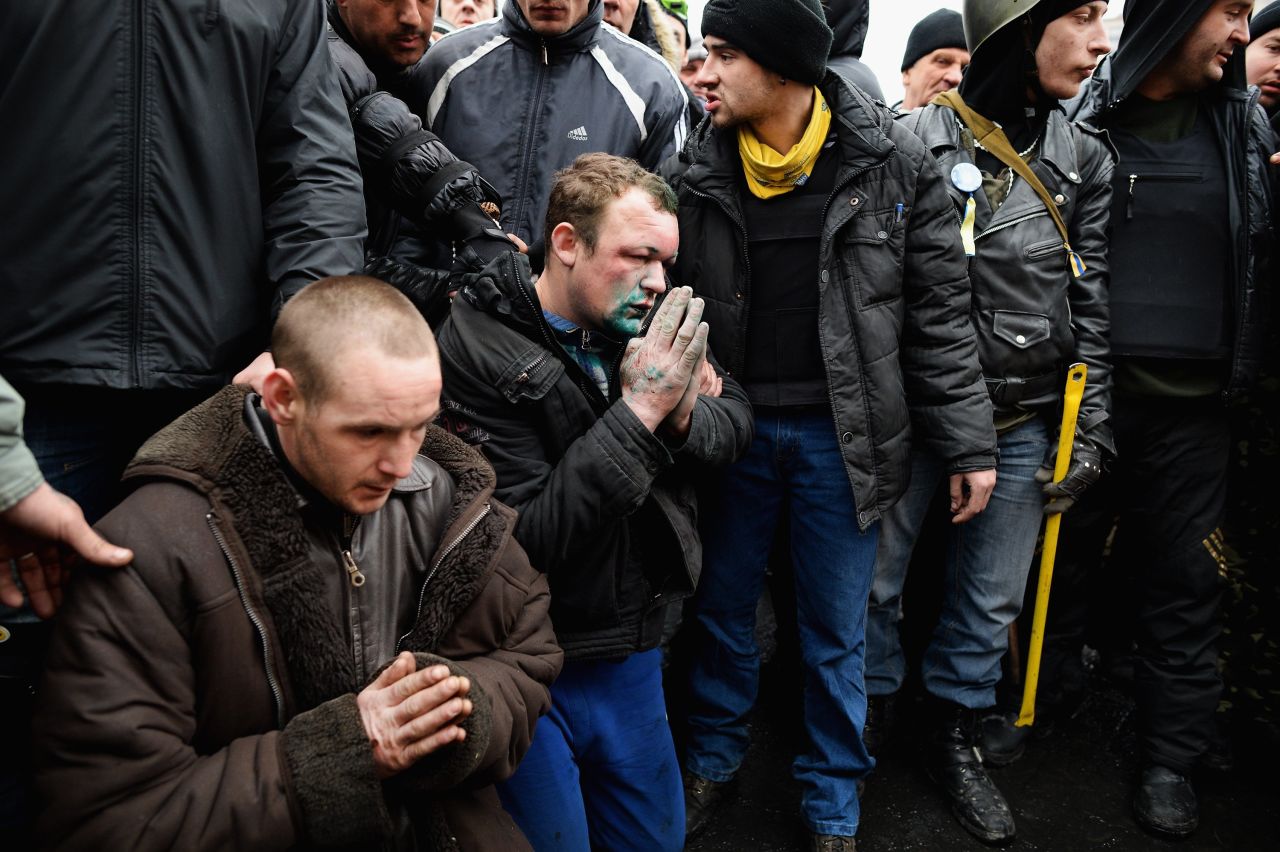 Two pro-government supporters are made to pray February 23 in front of a shrine to dead anti-government protesters.