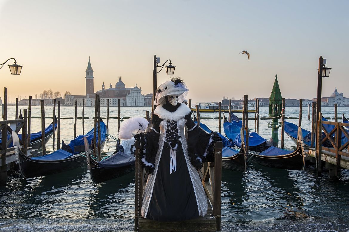 FEBRUARY 25 - VENICE, ITALY: A woman dressed in carnival costume poses in front of gondolas in Saint Mark's Square. The 2014 Carnival of Venice will run from February 15 to March 4 and includes a program of gala dinners, parades, dances, masked balls and music events. 