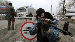 One of the armed masked men who call themselves members of Ukraine's disbanded elite Berkut riot police force aims his Klashnikov rifle at a checkpoint under a Russian national (L) and Russian naval (R) flags on a highway that connect Black Sea Crimea peninsula to mainland Ukraine near the city of Armyansk, on February 28, 2014. The spiralling tensions in a nation torn between the West and Russia took today a severe new turn when Ukraine's interim president Oleksandr Turchynov accused Russian soldiers and local pro-Kremlin militia of staging raids on Crimea's main airport and another base on the southwest of the peninsula where pro-Moscow sentiments run high.