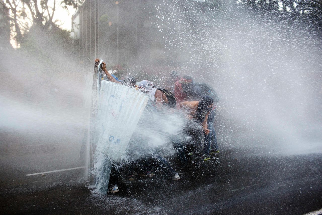 Protesters take cover from a police water cannon in Caracas on February 28.