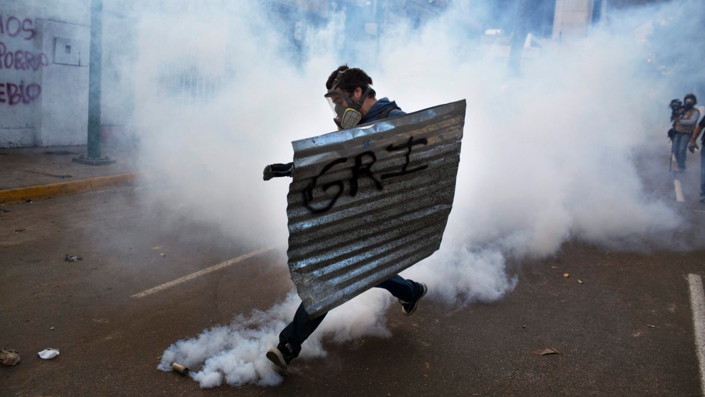 A masked protester with a makeshift shield kicks a tear gas canister launched by the National Guard during clashes in Caracas on Sunday, March 2.