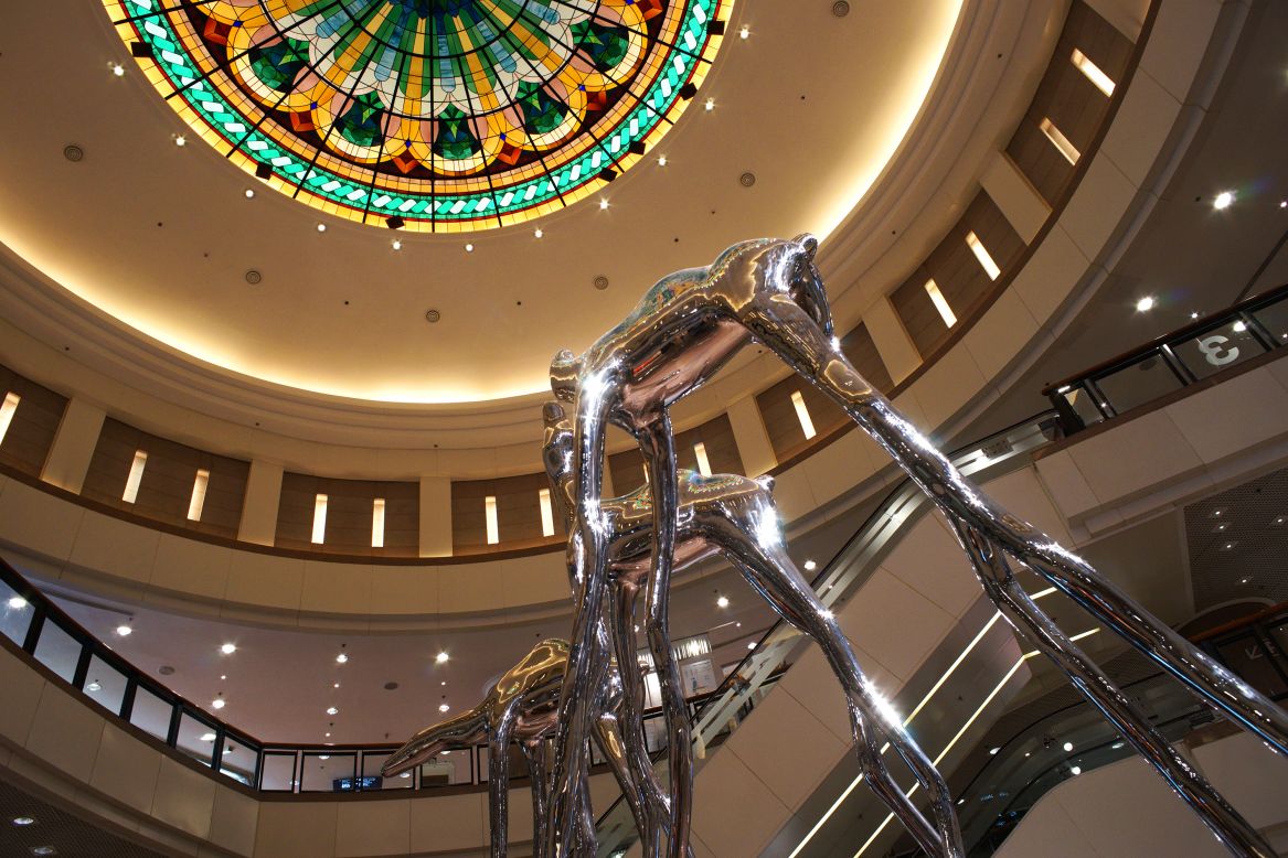 In the atrium of Harbour City's Gateway Arcade, three stainless steel camels stand five meters tall. The disproportionate size of the long skinny legs against the camels' bodies expresses the human desire for long journeys.