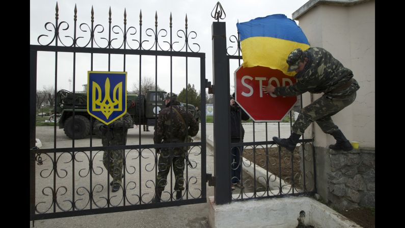 A Ukrainian airman puts the Ukrainian national flag over the gate of the Belbek air base as they guard what's left under their control on March 4.