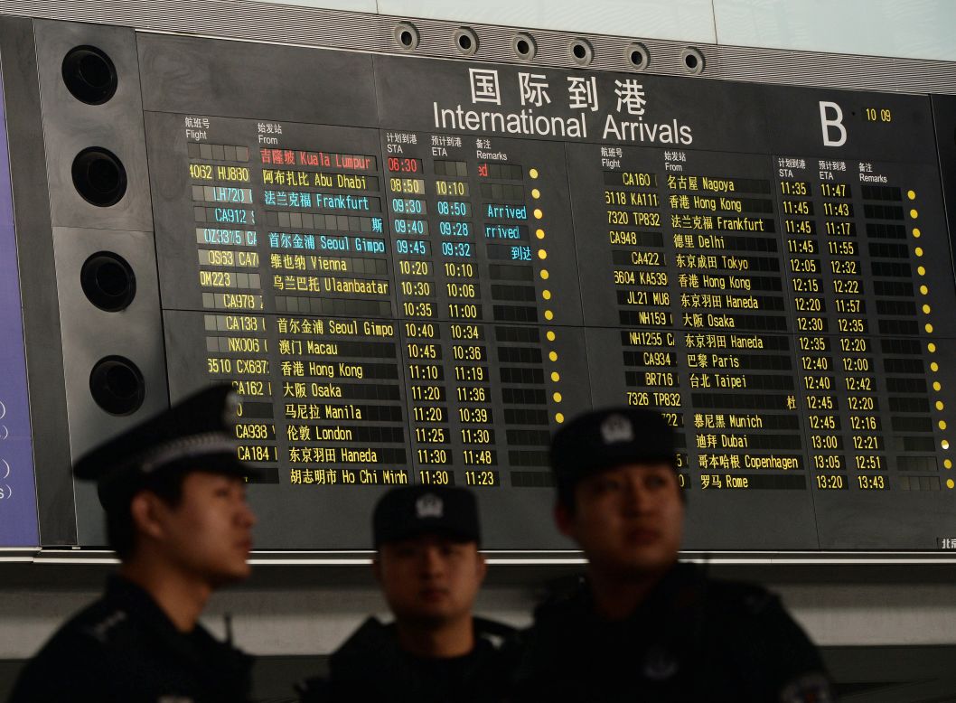 Chinese police at the Beijing airport stand beside the arrival board showing delayed Flight 370 in red on March 8, 2014.