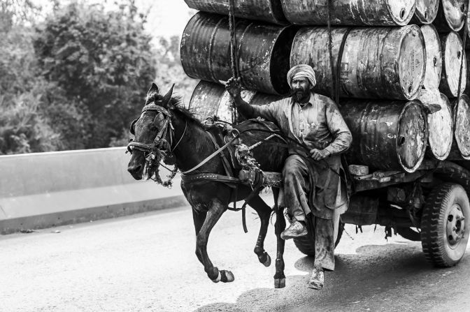 A man drives his horse at full tilt down a dual carriageway with a large load of empty water barrels in Faisalabad, Pakistan.