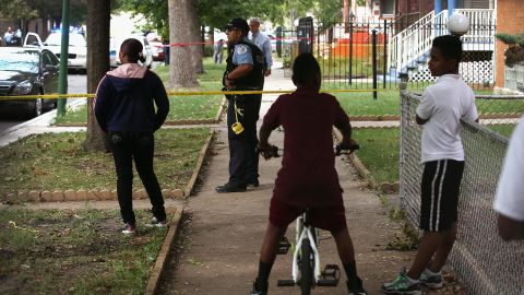 Family and friends watch police investigate the scene where a 14-year-old boy was shot and killed in September.
