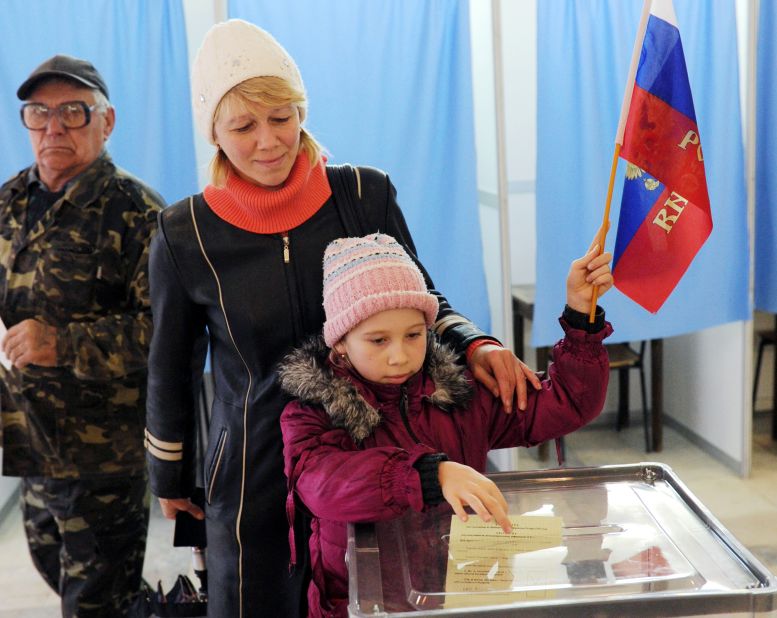 A child casts her mother's ballot March 16 while holding a Russian flag at a polling station in Simferopol.