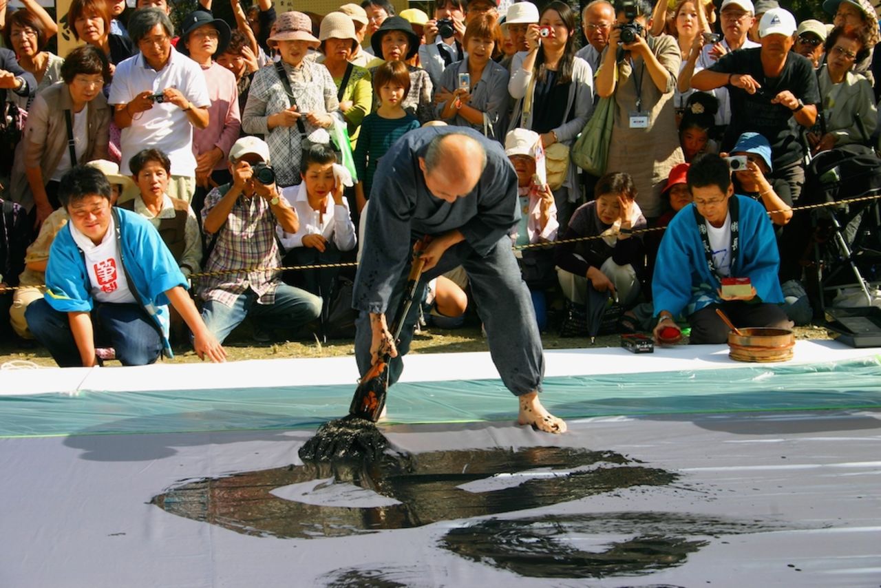 Calligraphy masters pace barefoot around a "canvas" (a large vinyl sheet spread on the ground) in a balletic whirl, wielding a heavy brush longer than their arm.