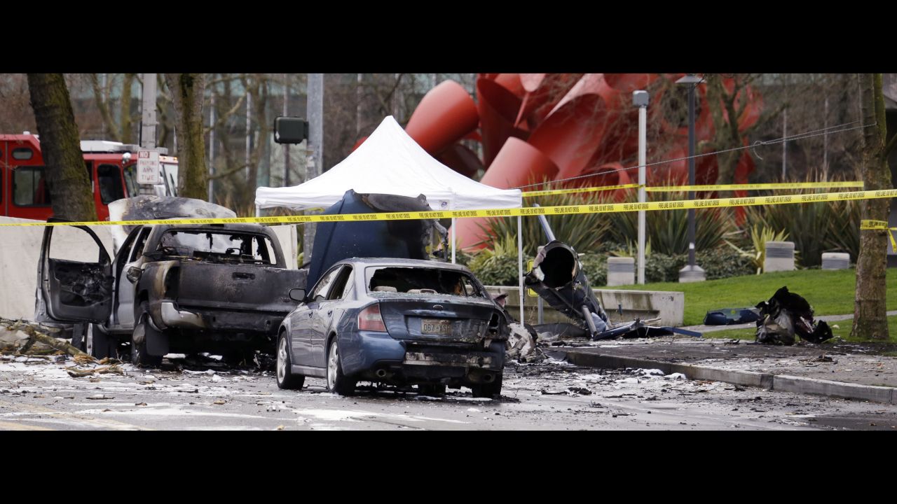 Caution tape surrounds the charred wreckage of a news helicopter and two vehicles after the helicopter crashed onto a street near Seattle's Space Needle on Tuesday, March 18. Both people inside the helicopter died, and a third person was critically injured on the ground, a spokesman for the Seattle Fire Department said.